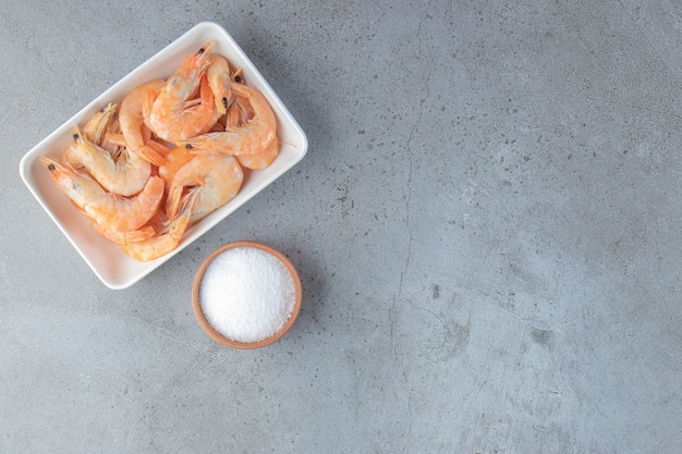 Tasty shrimps in a bowl next to salt, on the marble background. 