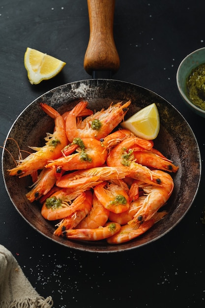Фото Вкусные креветки со специями и соусом на сковороде на темной поверхности