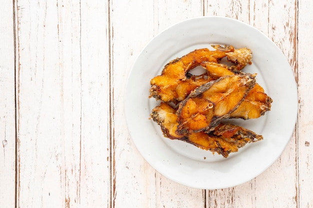 Foto gustosa fetta di pesce fritto di tilapia del nilo in cerchio bianco piatto di ceramica su sfondo bianco struttura di legno con copia spazio per testo piano tavolo vista piatta