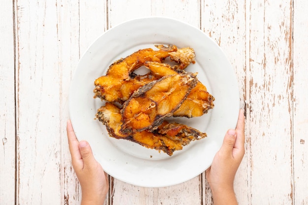 Tasty slice fried nile tilapia fish in white circle ceramic plate with hands on white wood texture background top table view flat lay