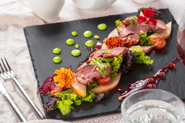 Tasty sliced roast duck breast with fresh vegetable salad closeup on a plate