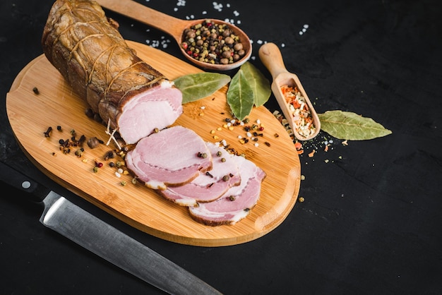 Tasty smoked ham with spices on black background. Copy space