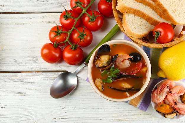 Tasty soup with shrimps, mussels, tomatoes and black olives in bowl on wooden background