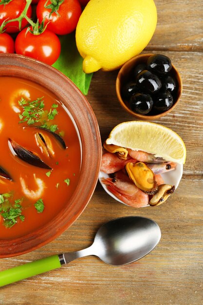 Photo tasty soup with shrimps mussels tomatoes and black olives in bowl on wooden background