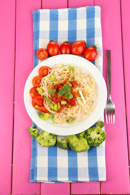 Tasty spaghetti with sauce and vegetables on plate on wooden table closeup