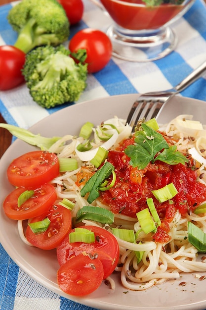 Tasty spaghetti with sauce and vegetables on plate on wooden table closeup