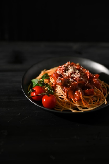 Tasty spaghetti with tomato sauce and parmesan cheese on a black plate and black background