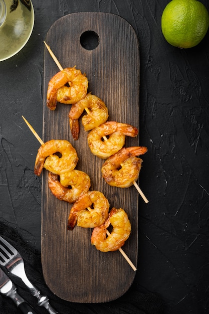 Tasty spiced shrimp skewers  sriracha kebabs with lime set, on wooden serving board, on black