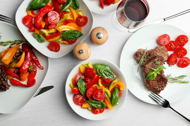 Tasty steak with vegetable salad and glass of wine on table