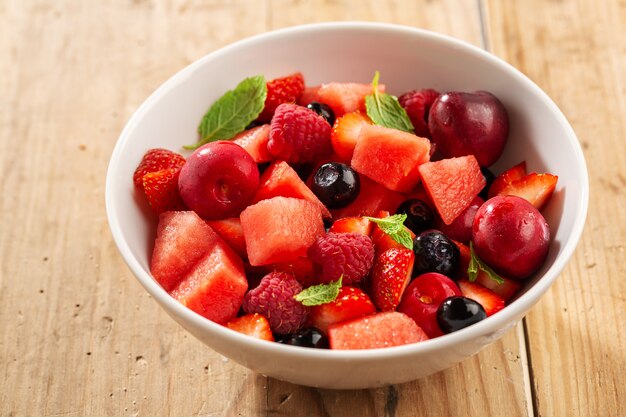 Tasty summer berries cut in bowl with mint. Closeup