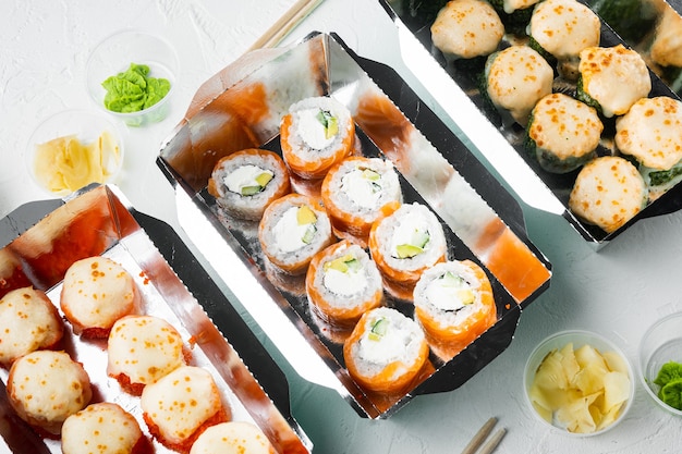Tasty sushi rolls in disposable boxes set, on white stone 
