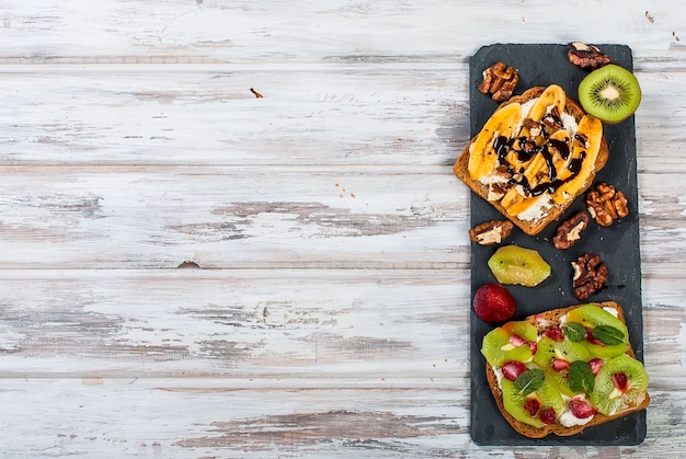 Tasty sweet sandwiches with bananas, nuts and chocolate, kiwi, strawberries and mint on wooden table 