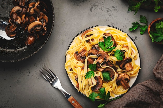 Фото Вкусная паста тальятелле с грибами, подаваемая на тарелке с петрушкой и специями на фоне серого каменного кухонного стола, вид сверху здоровая веганская кухня и концепция итальянской кухни