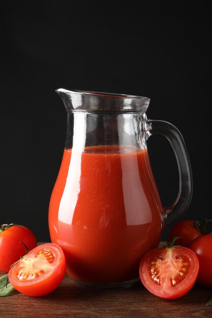 tasty tomato juice in jug and vegetables on wooden table against black background