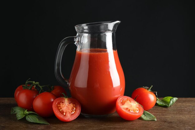 tasty tomato juice in jug and vegetables on wooden table against black background