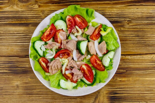 Tasty tuna salad with lettuce and fresh vegetables on wooden table Top view