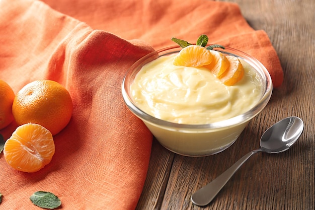 Tasty vanilla pudding with tangerine in bowl on table