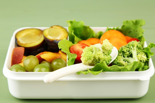 Tasty vegetarian food in plastic box on green wooden table