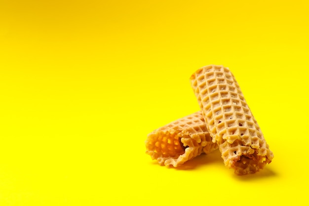 Tasty wafer rolls with condensed milk on yellow background