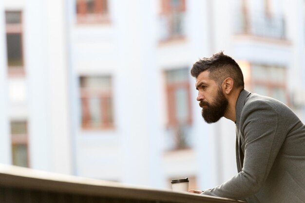 A tasty way to start his day. Businessman in hipster style holding takeaway coffee. The best time of day to drink coffee. Hipster with paper cup walking in city. Bearded man enjoying morning coffee.