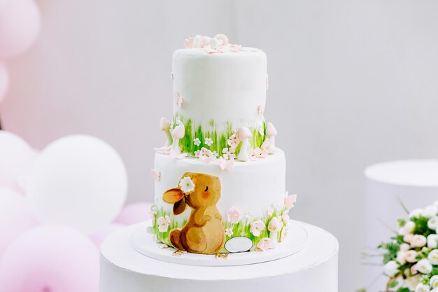 사진 풍선이 있는 파스텔 색 배경 앞에 있는 어린 소녀의 맛있는 흰색 생일 케이크