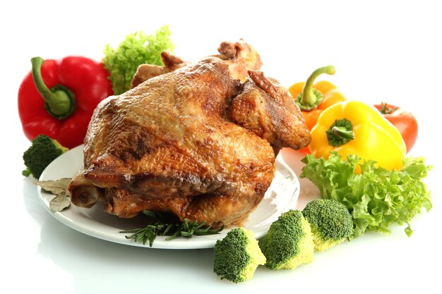 Tasty whole roasted chicken on plate with vegetables isolated on white