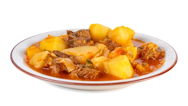 Tasty winter stew with meat and vegetables on a plate with ingredients isolated on white background.