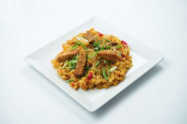 Tasty wok rice in sweet and sour sauce with vegetables and pork meat in a white plate on a gray table. Close up iew. Asian cuisine