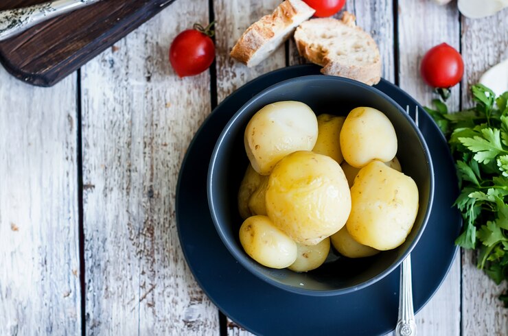 Фотография вкусный молодой вареный картофель с укропом, зеленью и луком в черной миске на белом деревенском деревянном столе