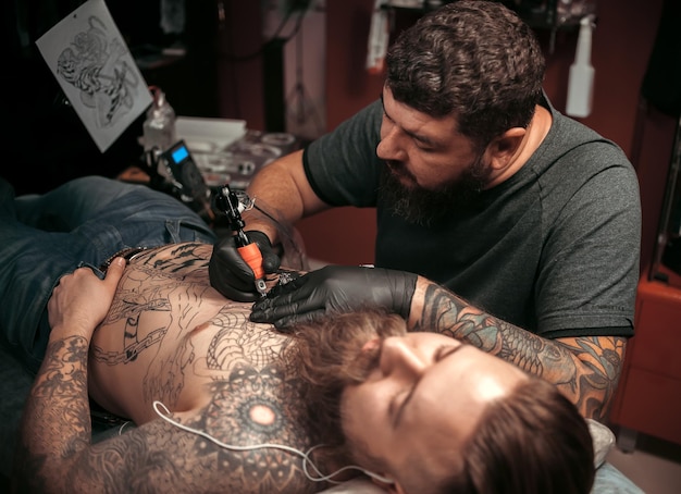 Tatoeëerder die een tatoeage maakt in een tattoo-salon./Professionele tattoo-artiest die een tattoo-afbeelding in de salon doet.