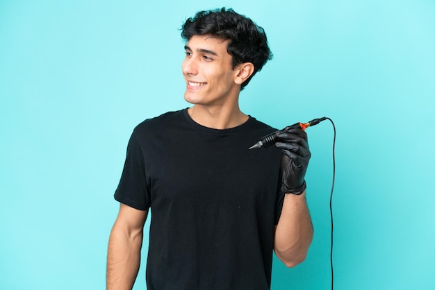 Tattoo artist Argentinian man isolated on blue background looking to the side and smiling