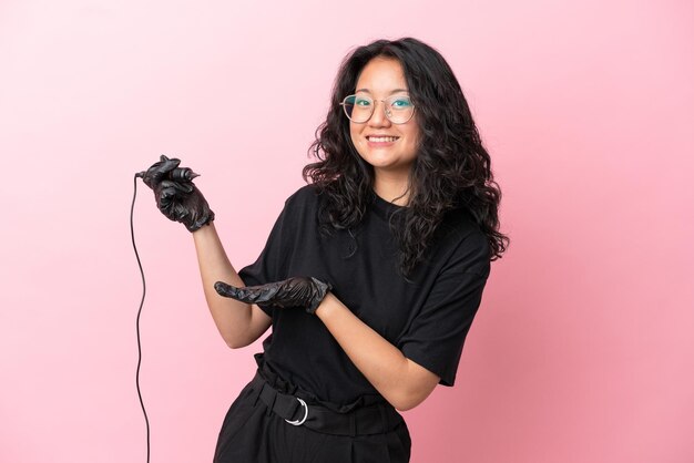 Tattoo artist asian woman isolated on pink background extending hands to the side for inviting to come