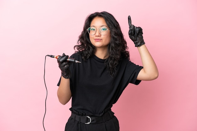 Tattoo artist asian woman isolated on pink background pointing up a great idea