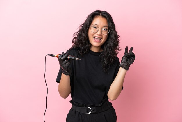 Tattoo artist asian woman isolated on pink background smiling and showing victory sign