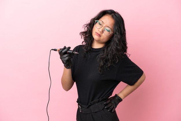 Tattoo artist asian woman isolated on pink background suffering from backache for having made an effort