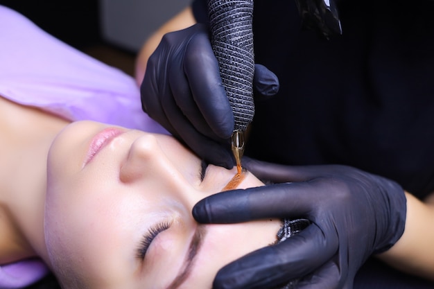 Tattoo artist in black gloves with a tattoo machine for applying pigment to the client's eyebrows