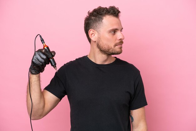 Tattoo artist brazilian man isolated on pink background looking to the side