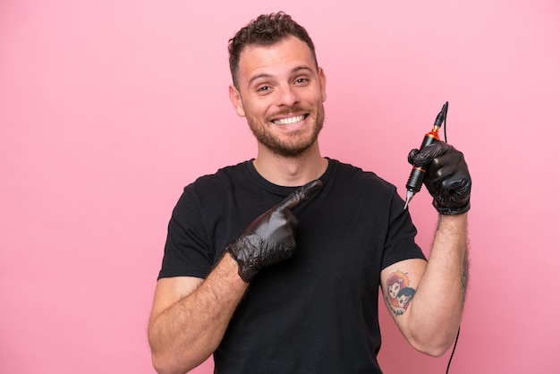 제품을 제시하기 위해 측면을 가리키는 분홍색 배경에 고립 된 문신 예술가 브라질 남자