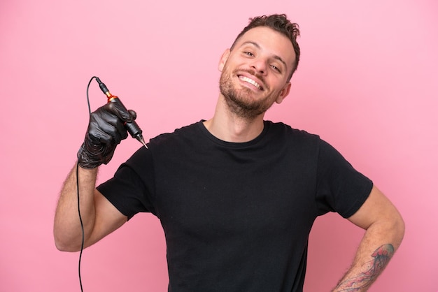 Tattoo artist brazilian man isolated on pink background posing with arms at hip and smiling