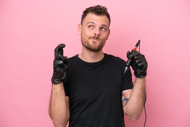 Tattoo artist brazilian man isolated on pink background with fingers crossing and wishing the best