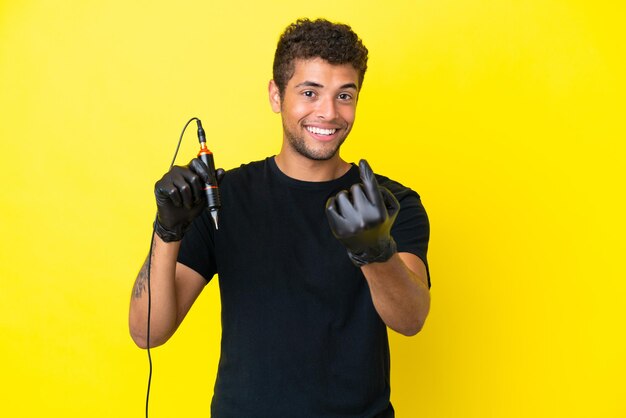 Tattoo artist Brazilian man isolated on yellow background doing coming gesture