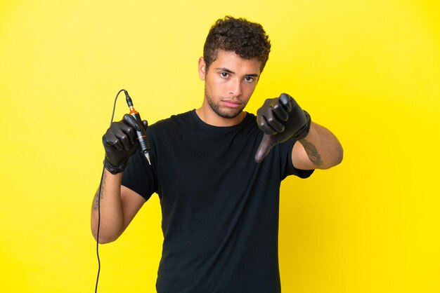 Tattoo artist Brazilian man isolated on yellow background showing thumb down with negative expression