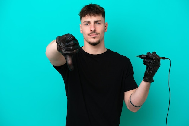 Tattoo artist caucasian man isolated on blue background showing thumb down with negative expression