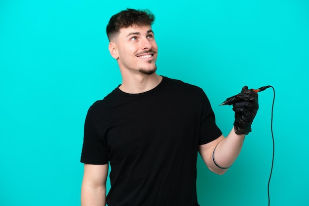 Tattoo artist caucasian man isolated on blue background thinking an idea while looking up