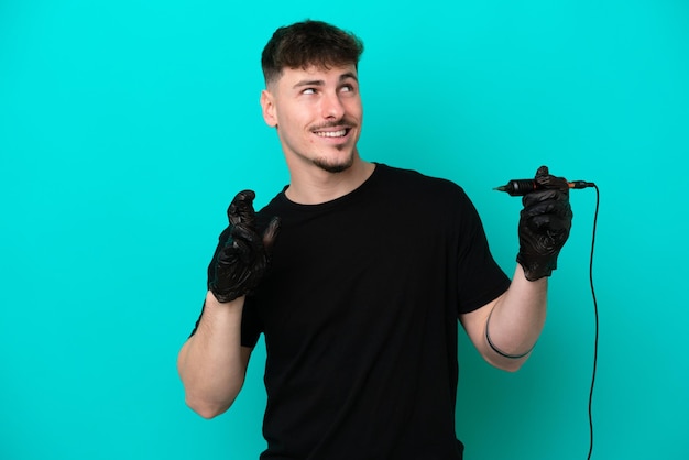 Tattoo artist caucasian man isolated on blue background with fingers crossing and wishing the best