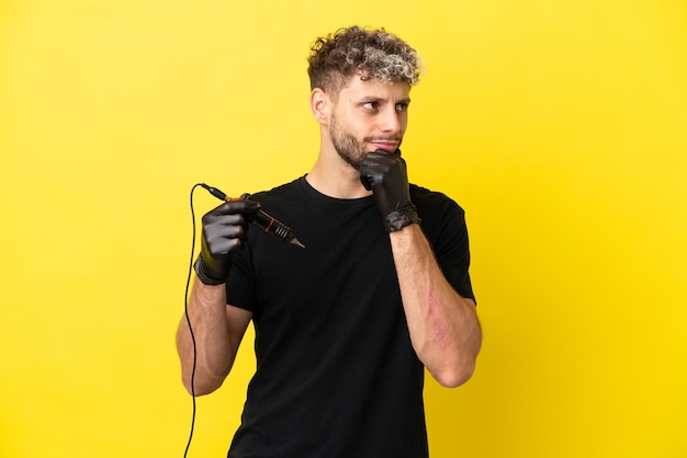 Tattoo artist caucasian man isolated on yellow background and looking up