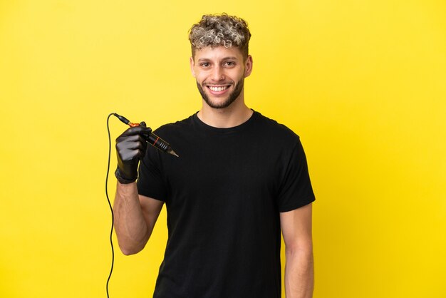 Tattoo artist caucasian man isolated on yellow background posing with arms at hip and smiling