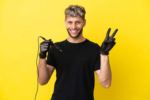 Tattoo artist caucasian man isolated on yellow background smiling and showing victory sign