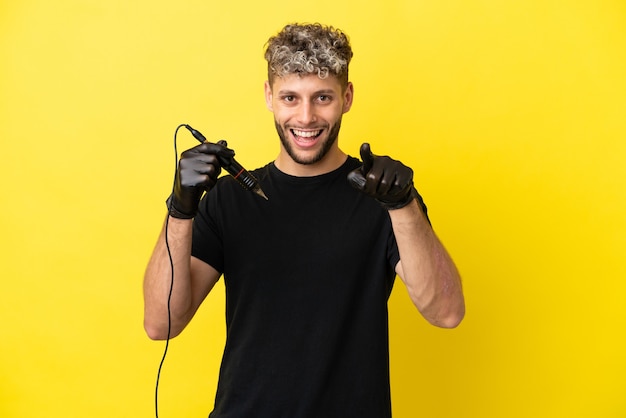 Tattoo artist caucasian man isolated on yellow background surprised and pointing front