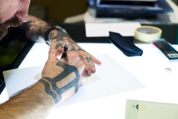 Foto tatuatore che progetta motivo sul tavolo luminoso in studio